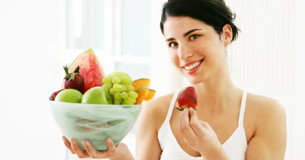 A woman at home eating one of the fruits listed for hydration