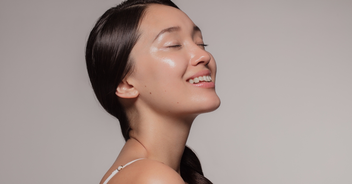 A woman withsmooth, clear, and glowing, suggesting a healthy or well-moisturized complexion, eyes closed smiling softly.